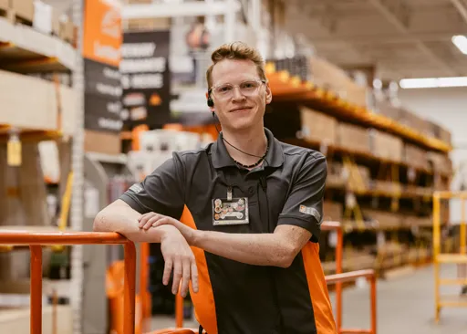 Home Depot associate smiling in lumber aisle, showcasing career growth opportunities