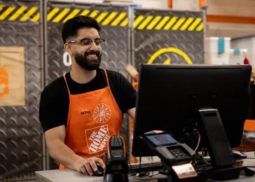 Home Depot Canada associate smiling while assisting customers at a store computer station, showing customer service and enthusiasm.